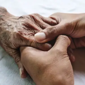 Close-up of a caregiver's hands gently holding the hand of an elderly person, symbolizing compassion, support, and care.