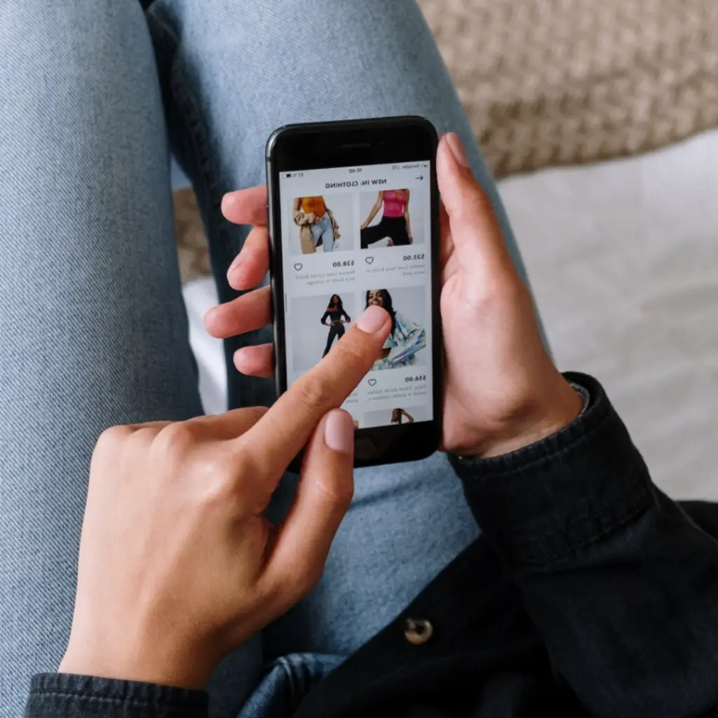 Close-up of a person browsing an online clothing store on a smartphone, showcasing a shopping interface with product images and prices, highlighting mobile e-commerce convenience.
