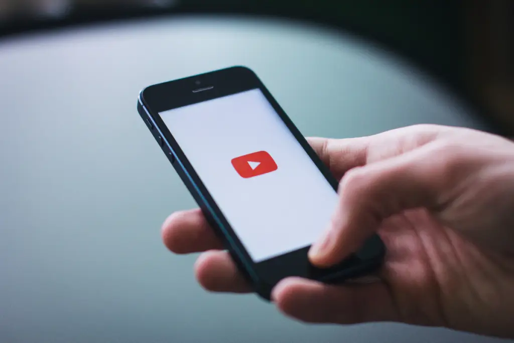 Close-up of a hand holding a smartphone with the YouTube app loading on the screen, symbolizing video marketing, YouTube advertising, and digital content promotion strategies.