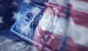 Close-up of U.S. hundred-dollar bills overlaid with rising arrows and percentage symbols, symbolizing increasing financial rates, tariffs, or economic pressure.